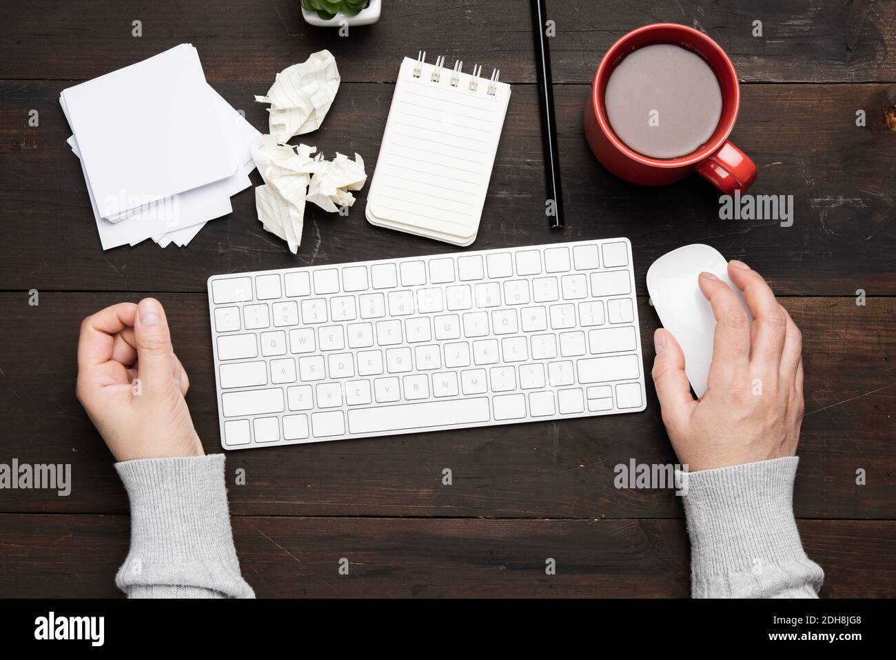white wireless keyboard and mouse on a wooden brown table, next to a white cup with coffee, top view Stock Photo