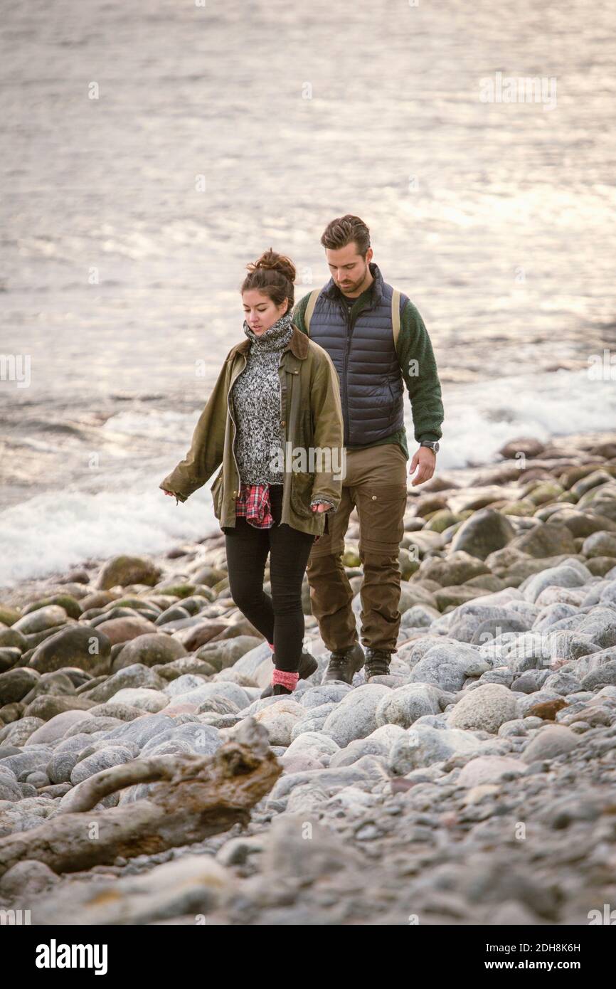 Couple walking on rocky shore during sunset Stock Photo