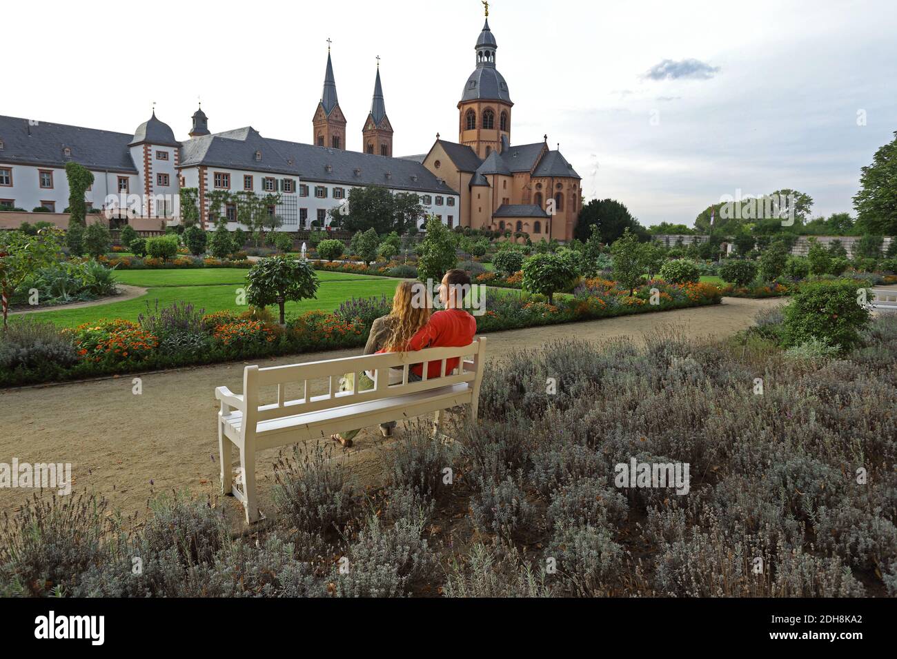 Young couple sitting on a bench and enjoy the convent garden and basilica in Seligenstadt on the Banks of the River Main, Germany Stock Photo