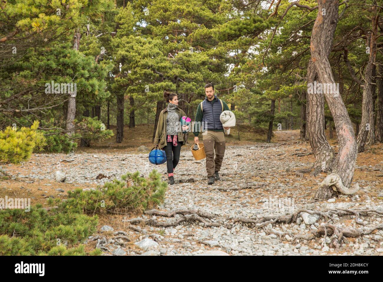 Couple carrying sleeping bags and basket in forest Stock Photo