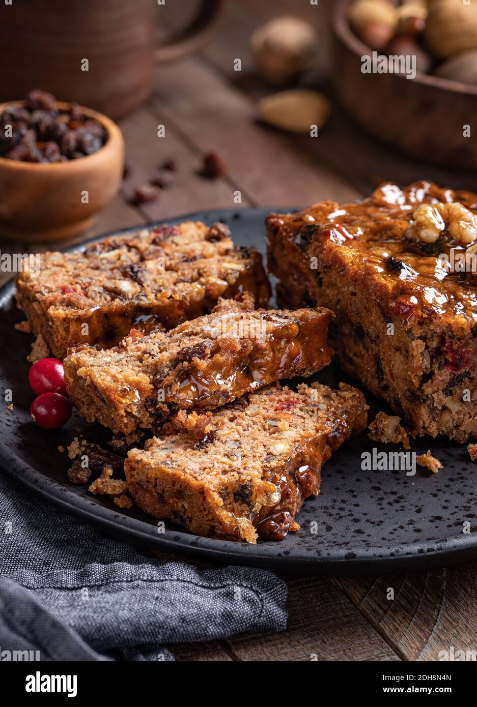 Fruitcake loaf sliced on a plate with raisins and nuts in background on a rustic wooden table Stock Photo
