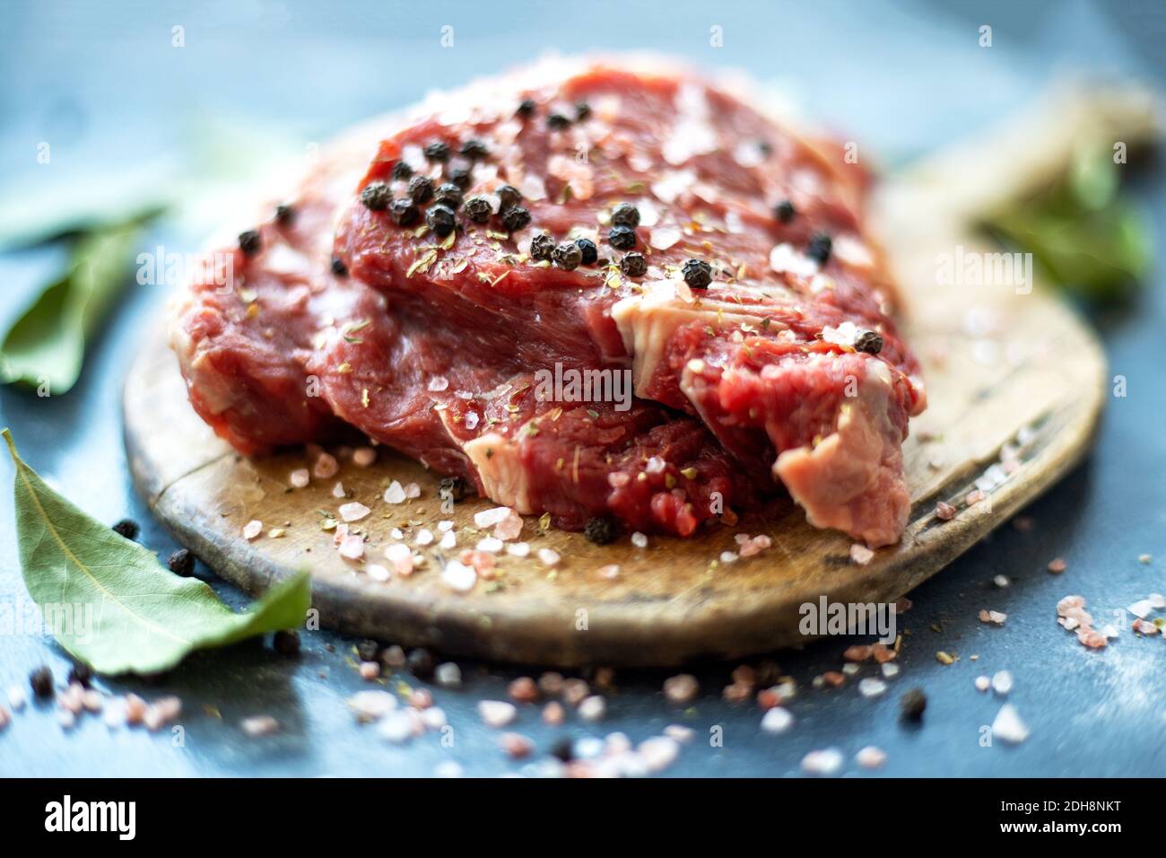 Raw meat beef steak on wooden cutting board, coarse pink Himalayan salt, black pepper, bay leaf