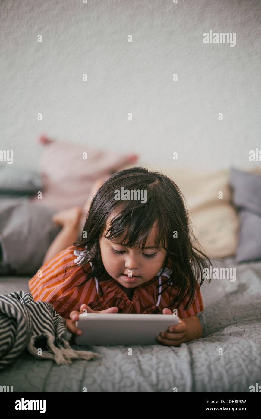 Down syndrome girl using digital tablet while lying on sofa at home Stock Photo