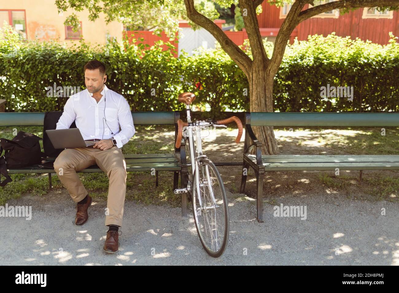 Businessman using laptop while sitting on park bench Stock Photo