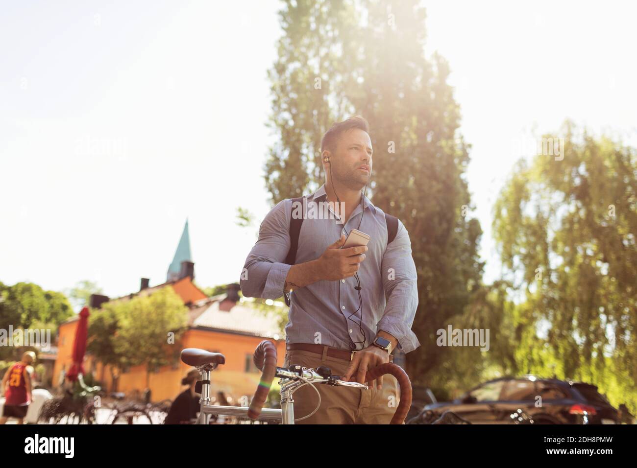 Low angle view of businessman holding bicycle and smart phone on sunny day Stock Photo