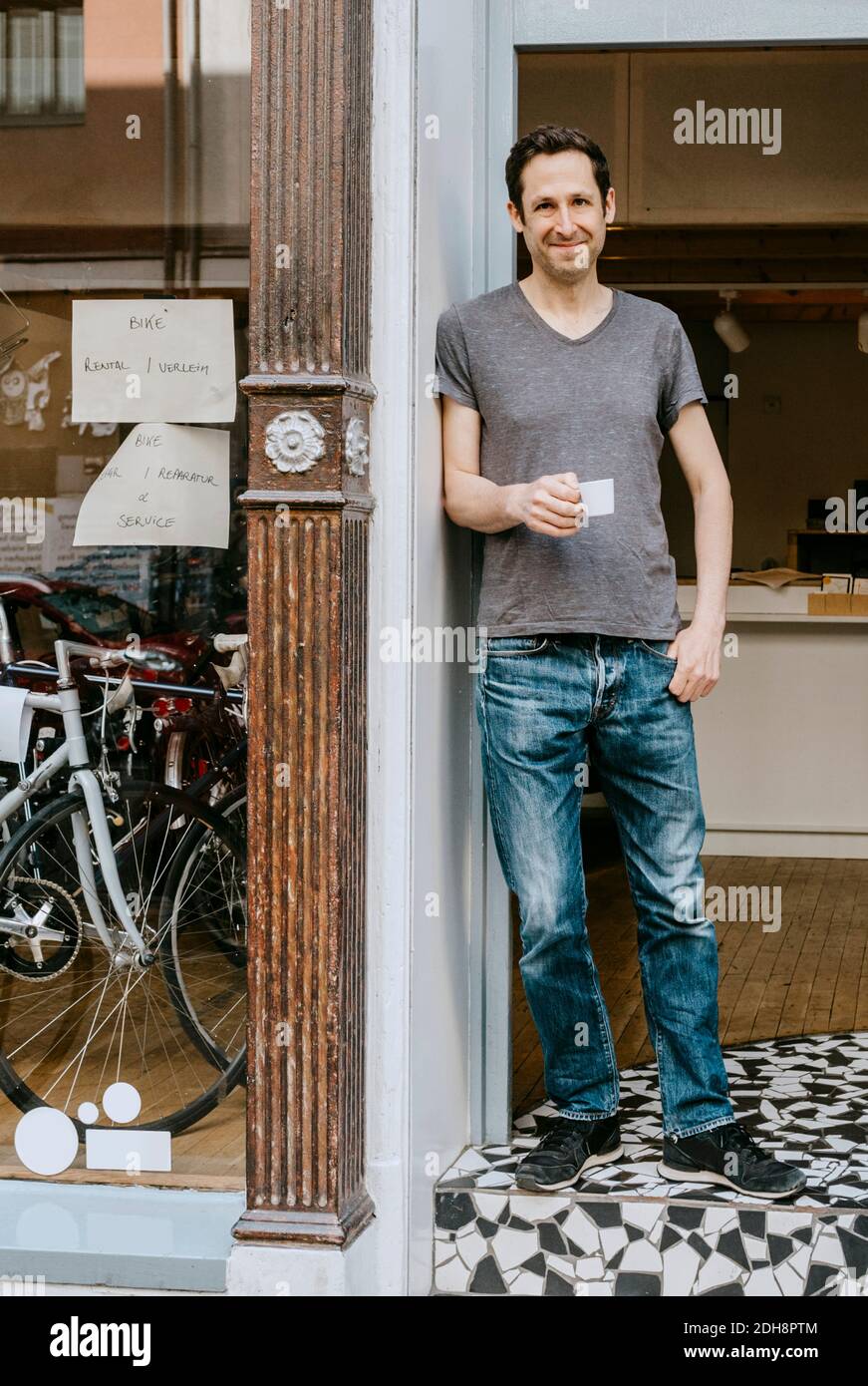 Portrait of smiling male owner with coffee cup standing in doorway of