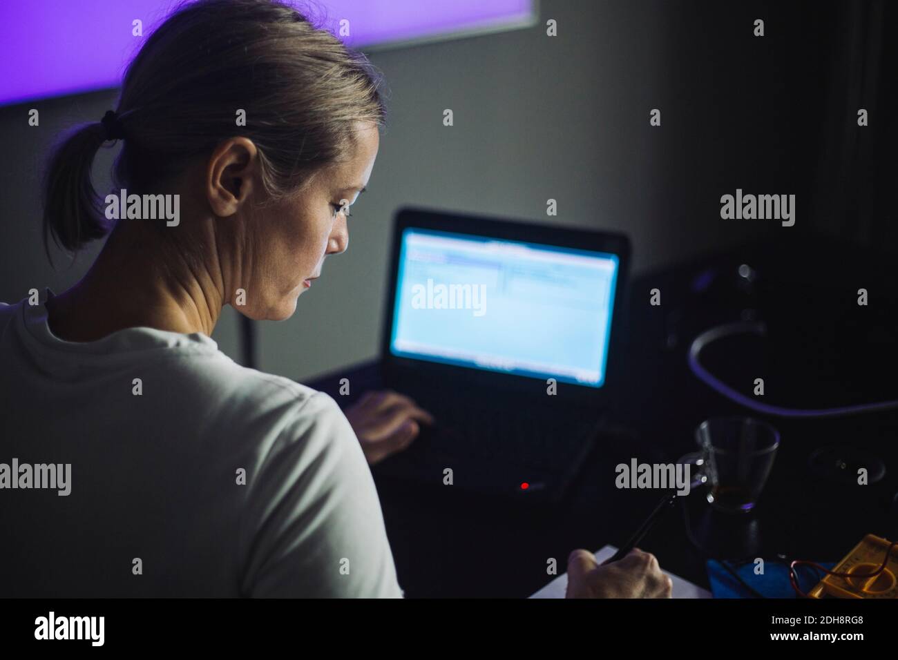 Female IT professional writing while working on laptop in creative office Stock Photo