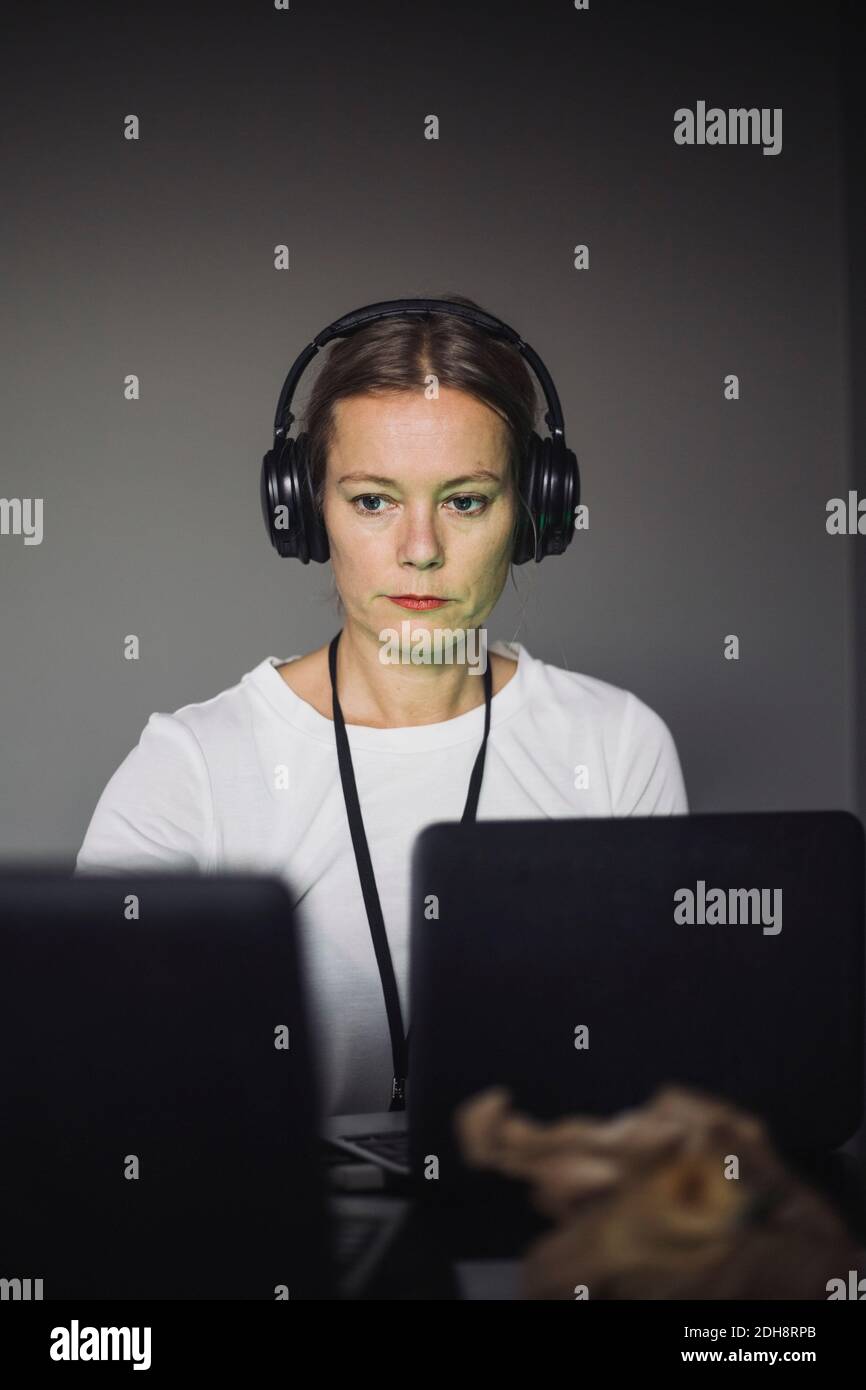 Female IT professional with headphones typing on laptop in creative office Stock Photo