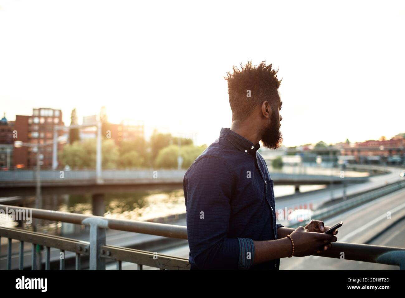 Young man with mobile phone standing on bridge against sky Stock Photo