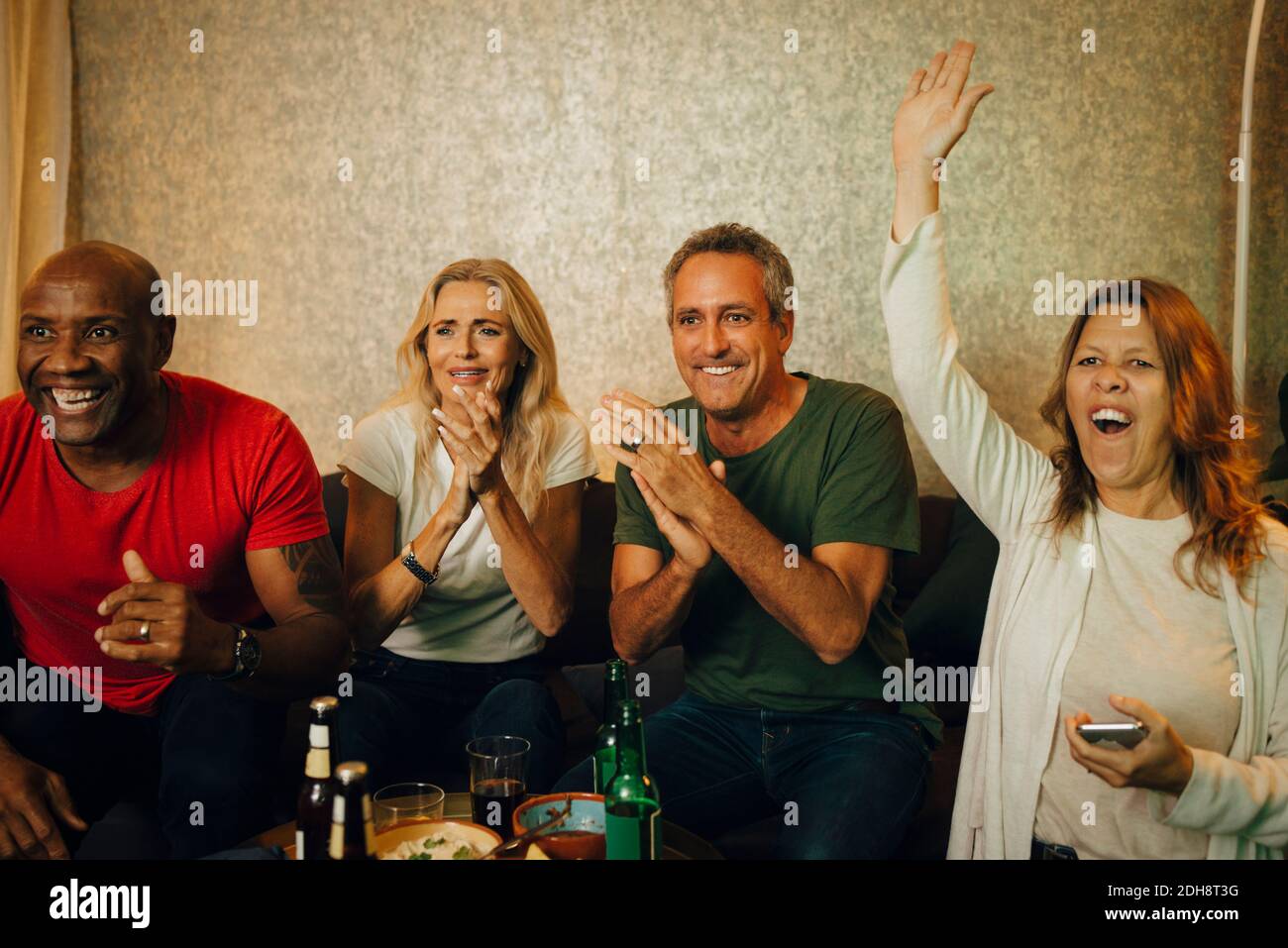 Cheerful woman with hand raised enjoying match with friends at night Stock Photo