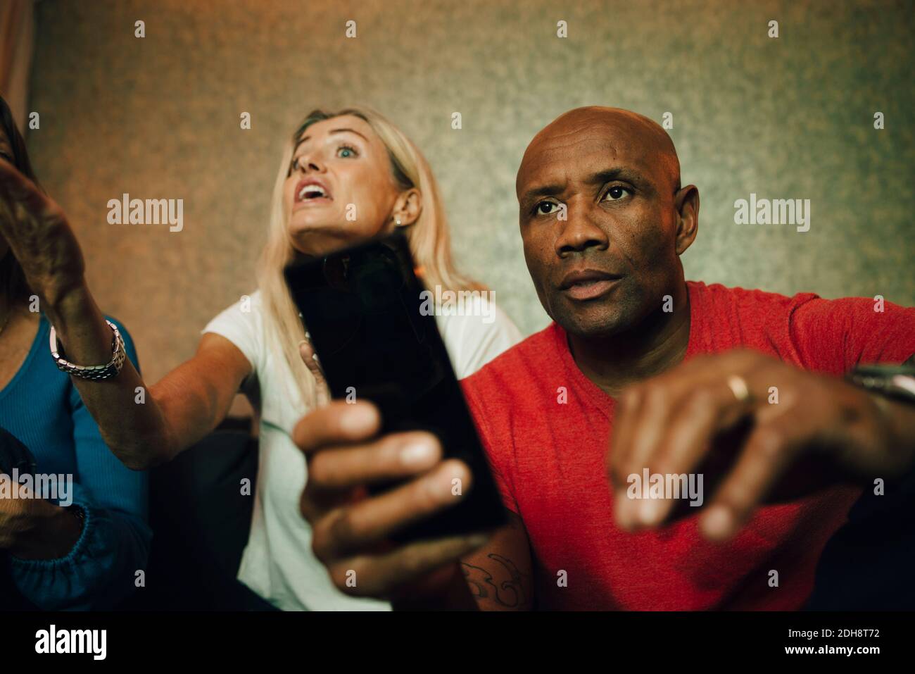Disappointed man sitting on sofa while woman talking in background during sporting event Stock Photo