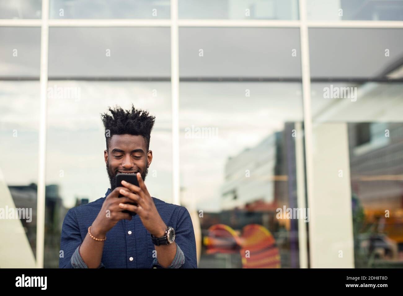 Happy young man using mobile phone against window Stock Photo