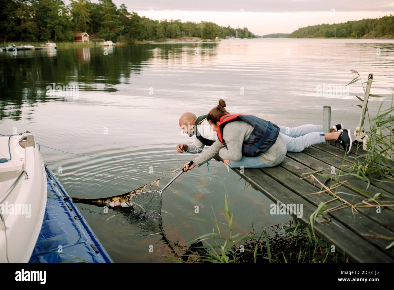 Smiling father helping daughter remove slipper from lake through fishing net Stock Photo