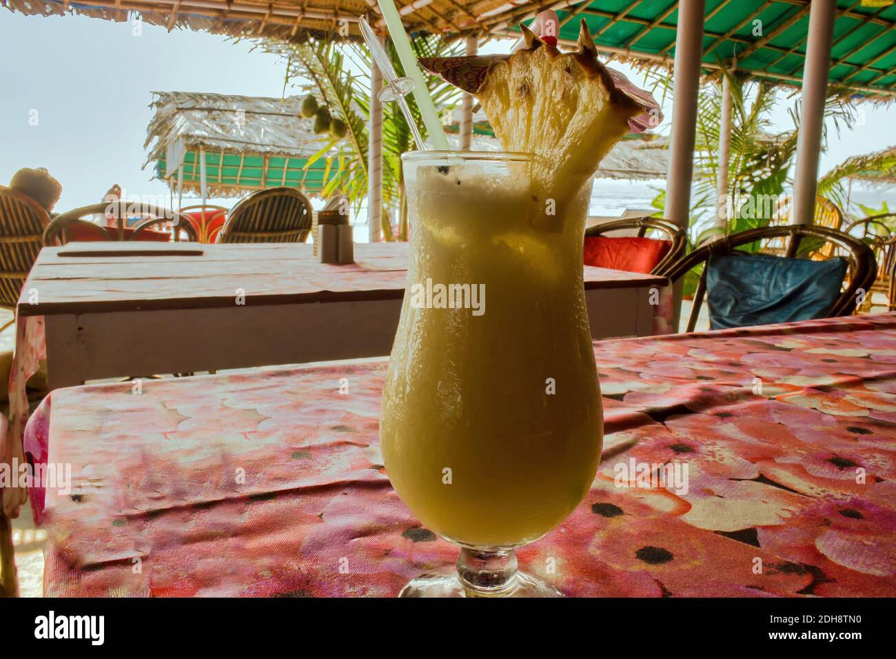 Pina colada cocktail with a pineapple garnish and a plastic straw on a table in an exotic location in Goa, India. Stock Photo