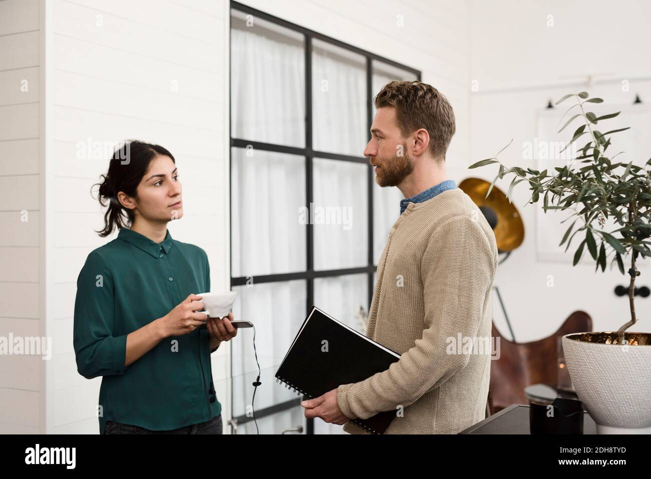 Businesswoman having coffee while talking to coworker at office Stock Photo