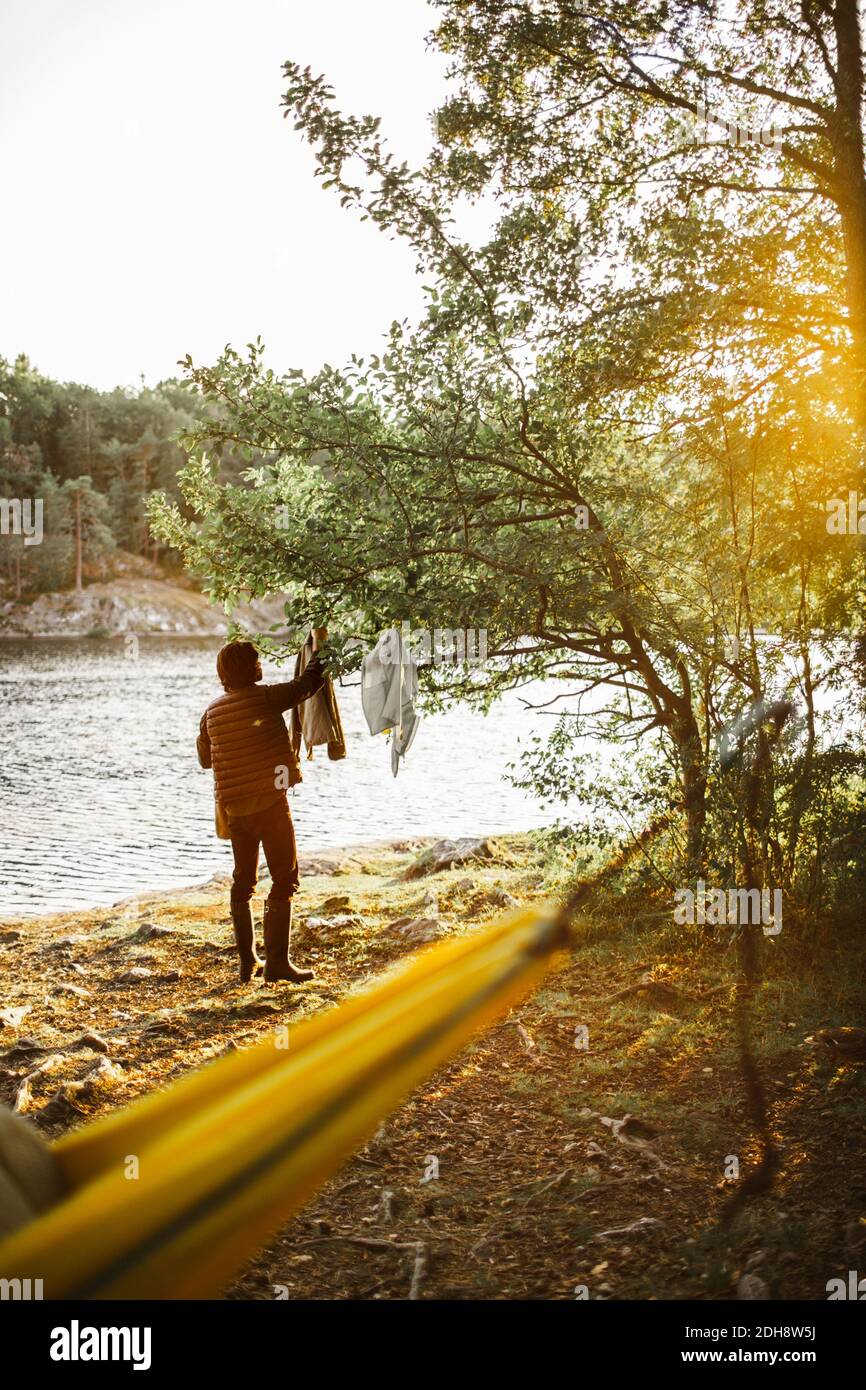 Young man hanging clothes on tree in forest during vacation Stock Photo