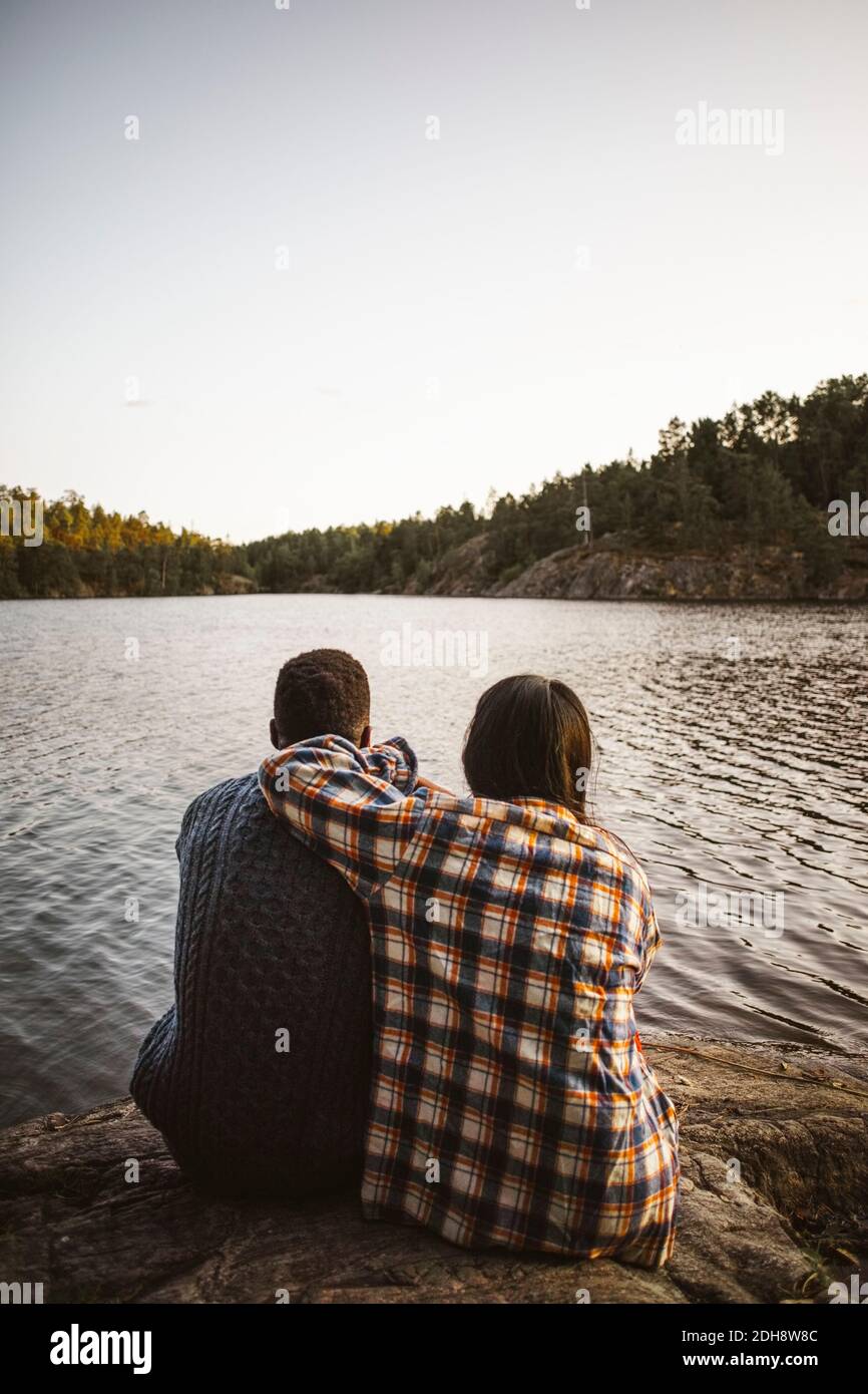 Rear view of man and woman sitting against lake in forest Stock Photo