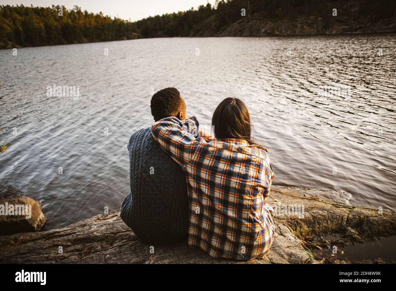Rear view of man and woman sitting by lake in forest Stock Photo