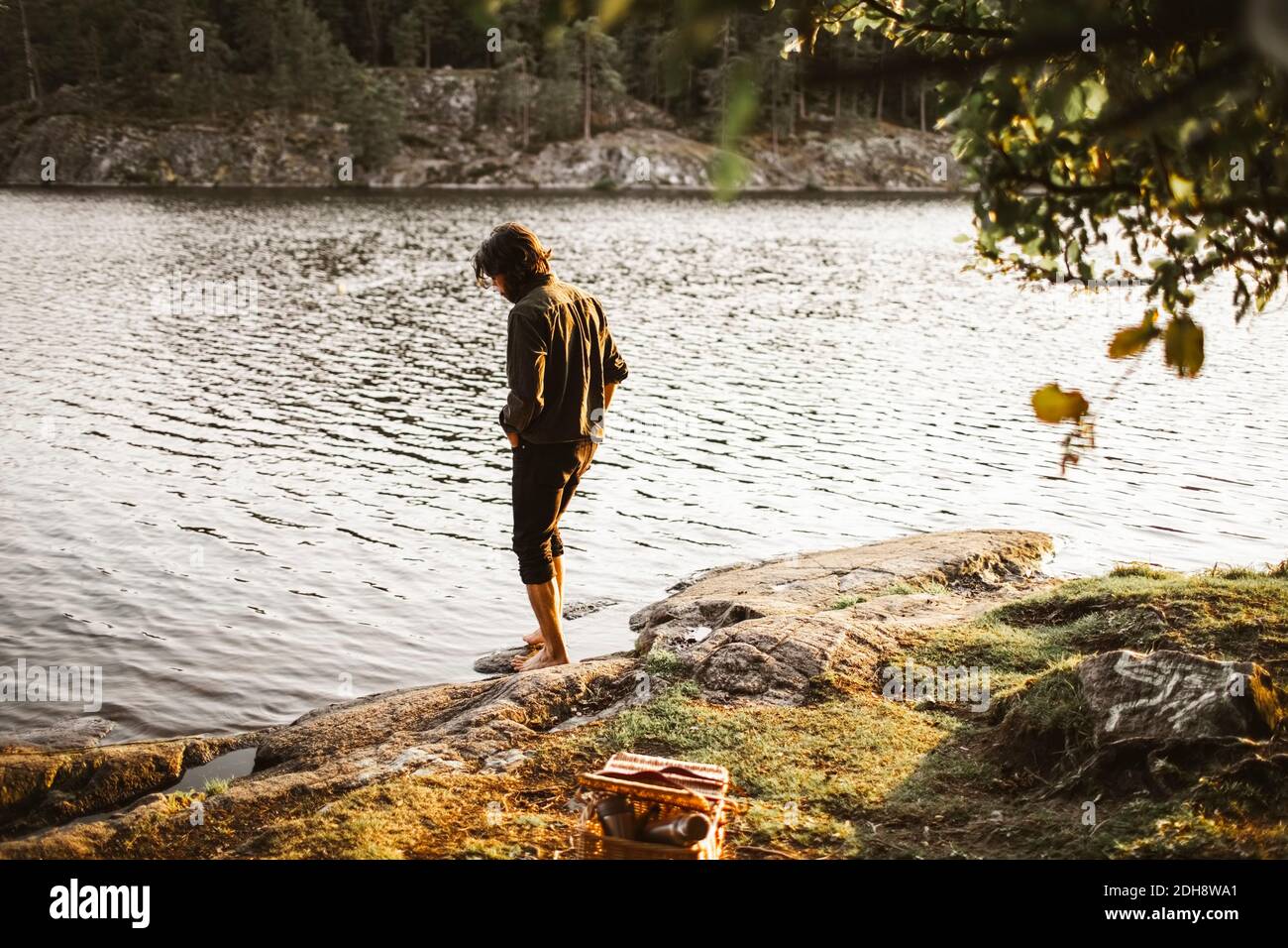 Young man standing by lake in forest during vacation Stock Photo