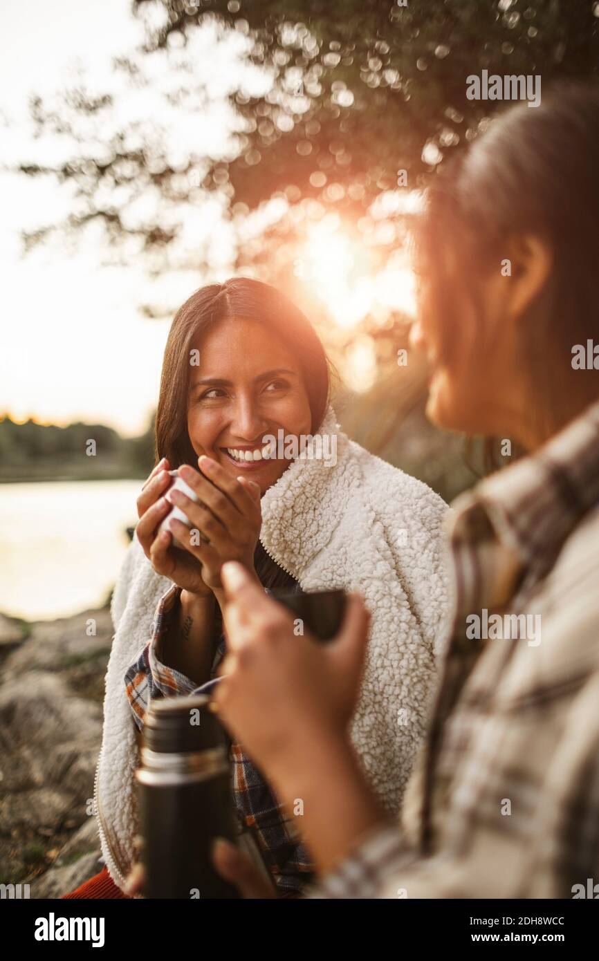 Smiling female friends talking while drinking coffee in forest Stock Photo