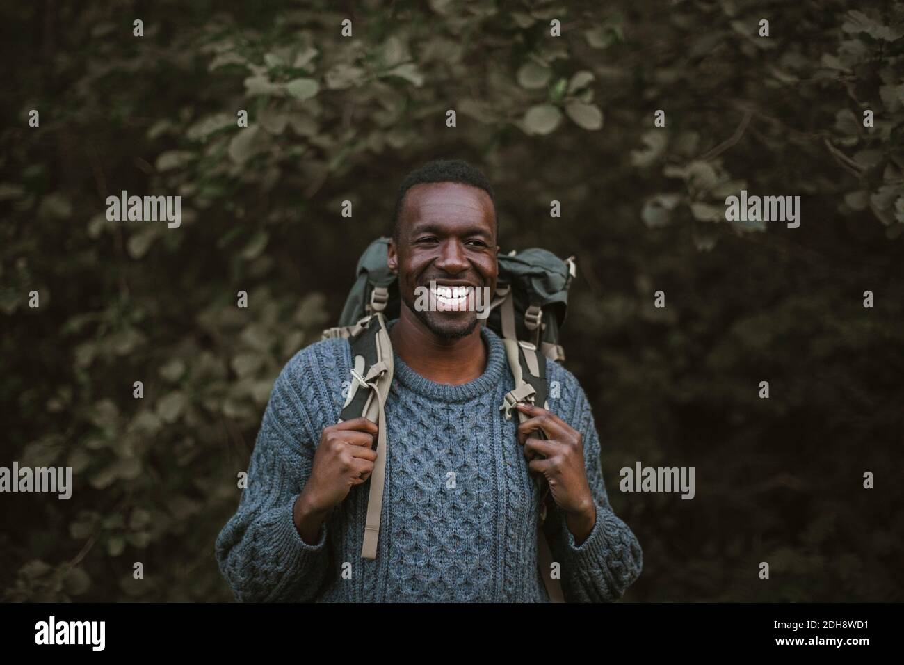 Smiling man with backpack standing in forest Stock Photo
