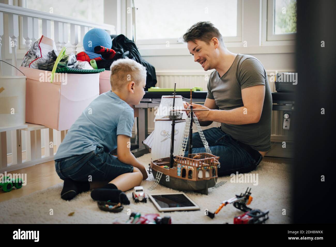 Smiling father and son making toy boat while sitting at home Stock Photo