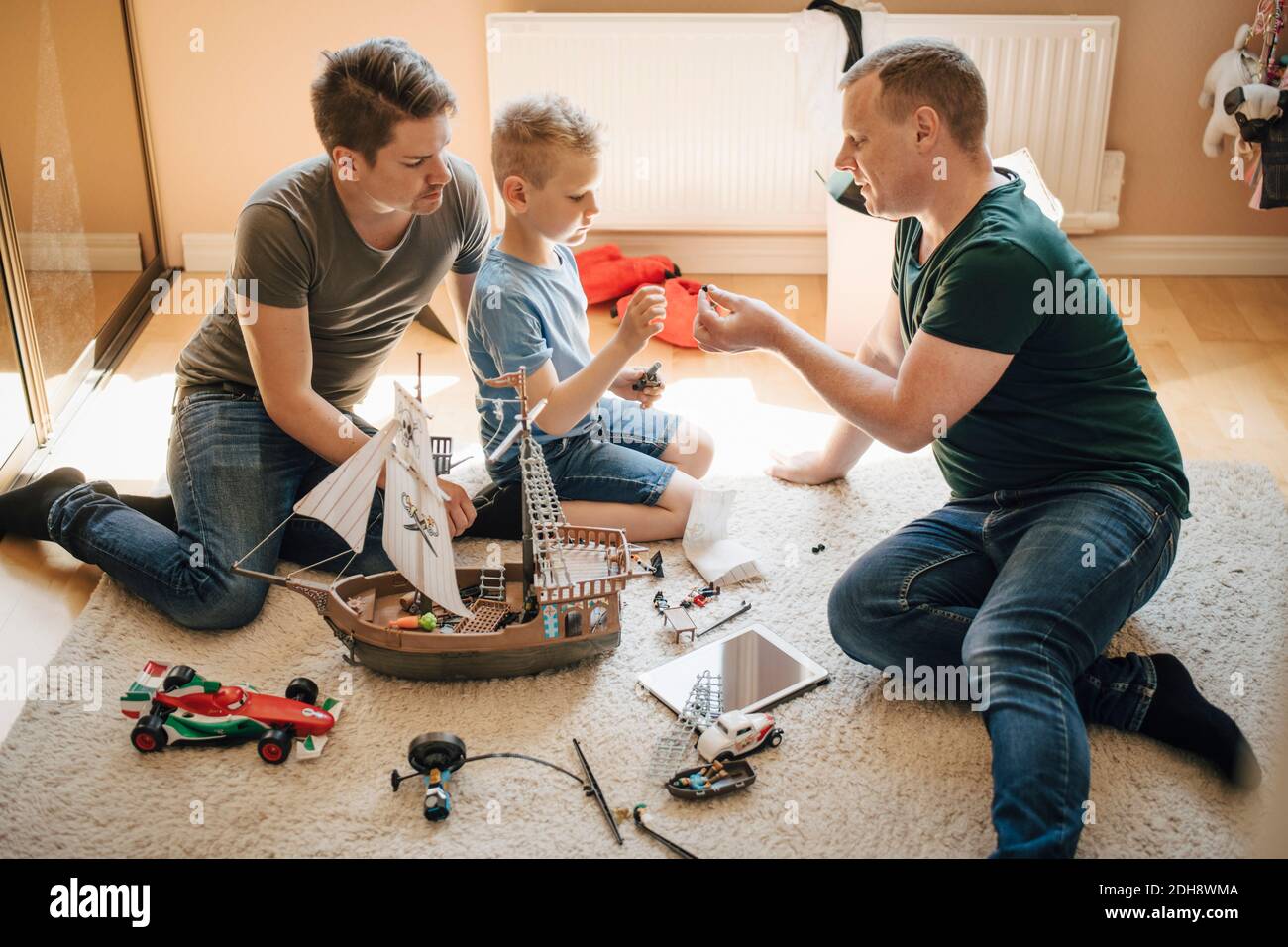 Side view of homosexual fathers and son making toy boat at home Stock Photo