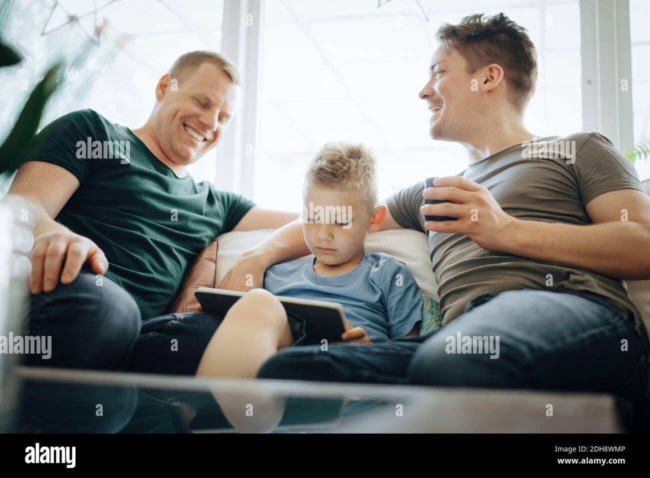 Smiling homosexual fathers talking while son using digital tablet at home Stock Photo