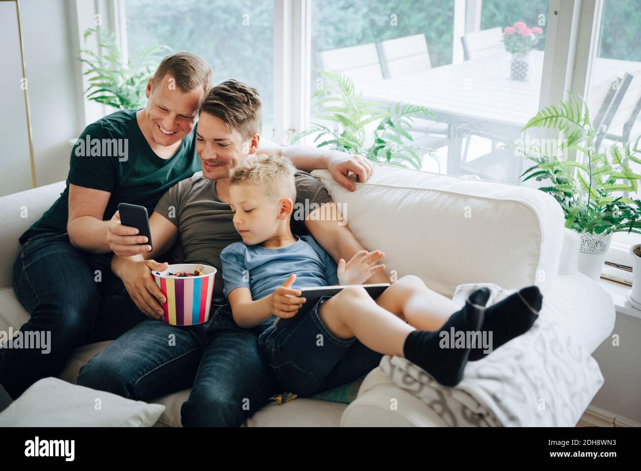 Smiling fathers with son using smart phone on sofa at home Stock Photo