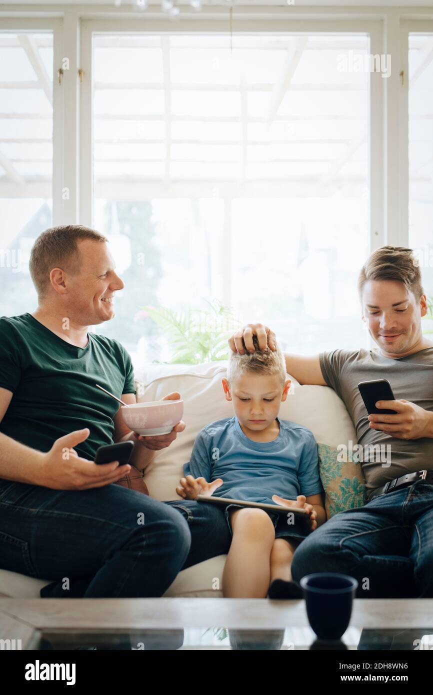 Smiling fathers talking while son using digital tablet at home Stock Photo