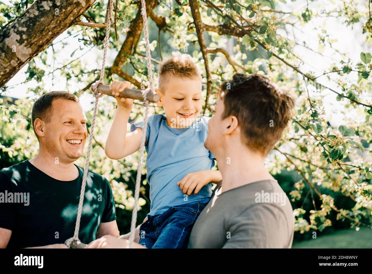 Homosexual fathers looking at smiling son playing in backyard Stock Photo