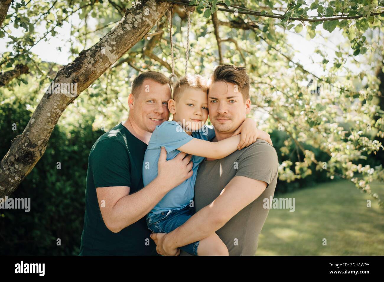 Portrait of homosexual fathers with son standing in backyard Stock Photo