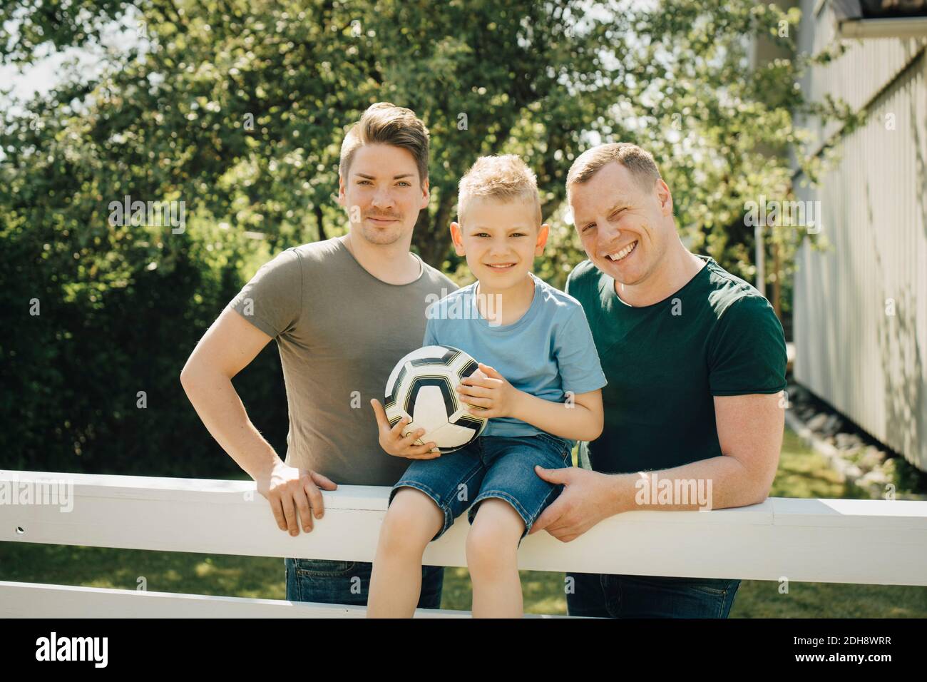 Portrait of homosexual fathers with son holding soccer ball in yard Stock Photo