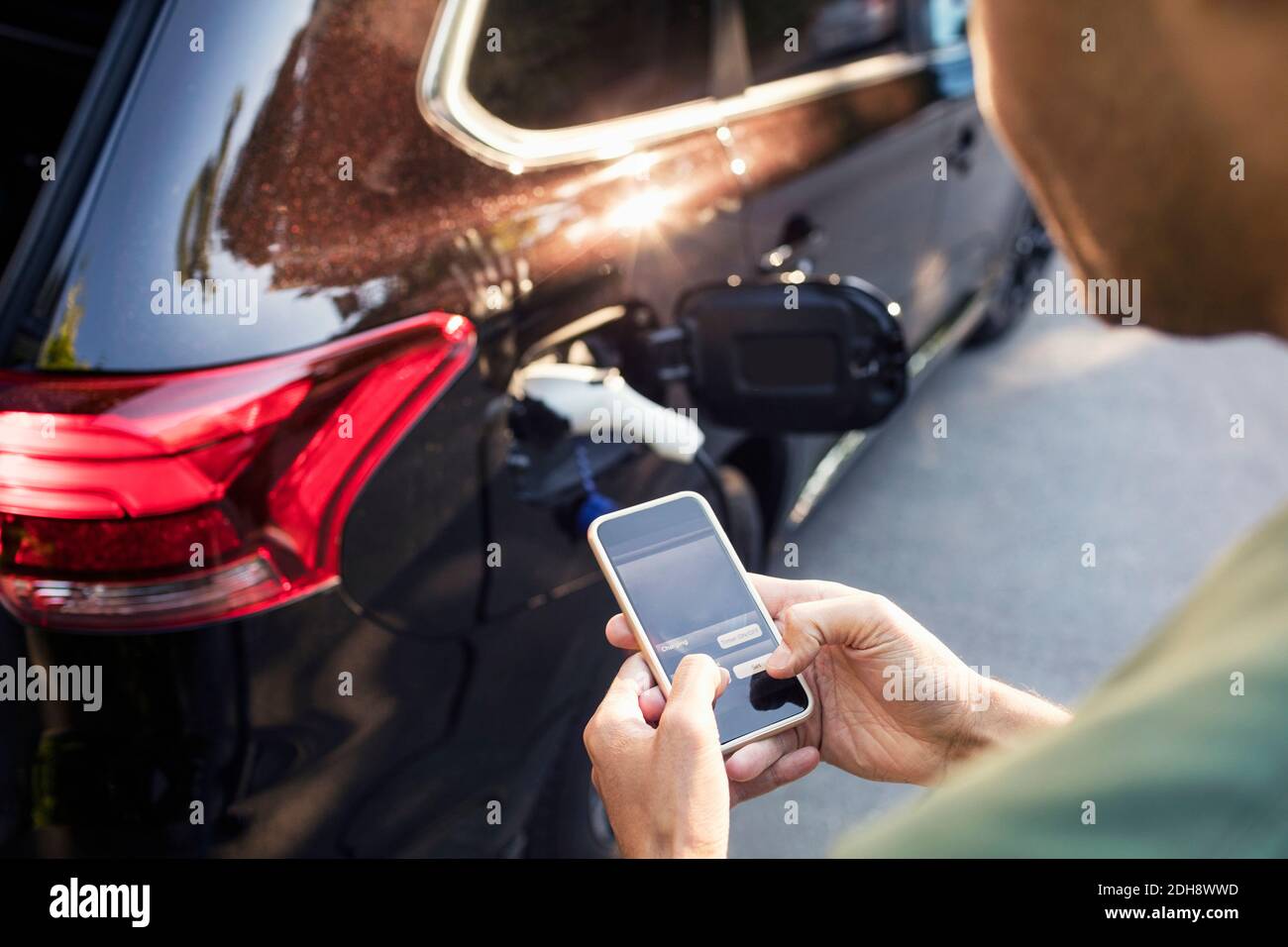 Man using mobile phone while standing by charging electric car Stock Photo