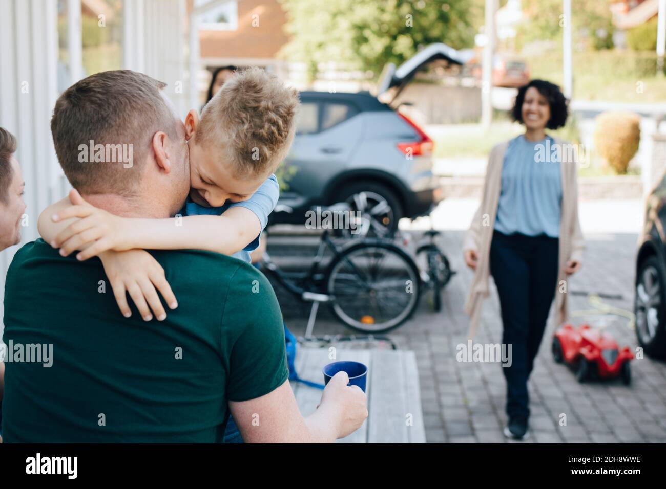 Rear view of father embracing son while woman walking towards house during weekend Stock Photo