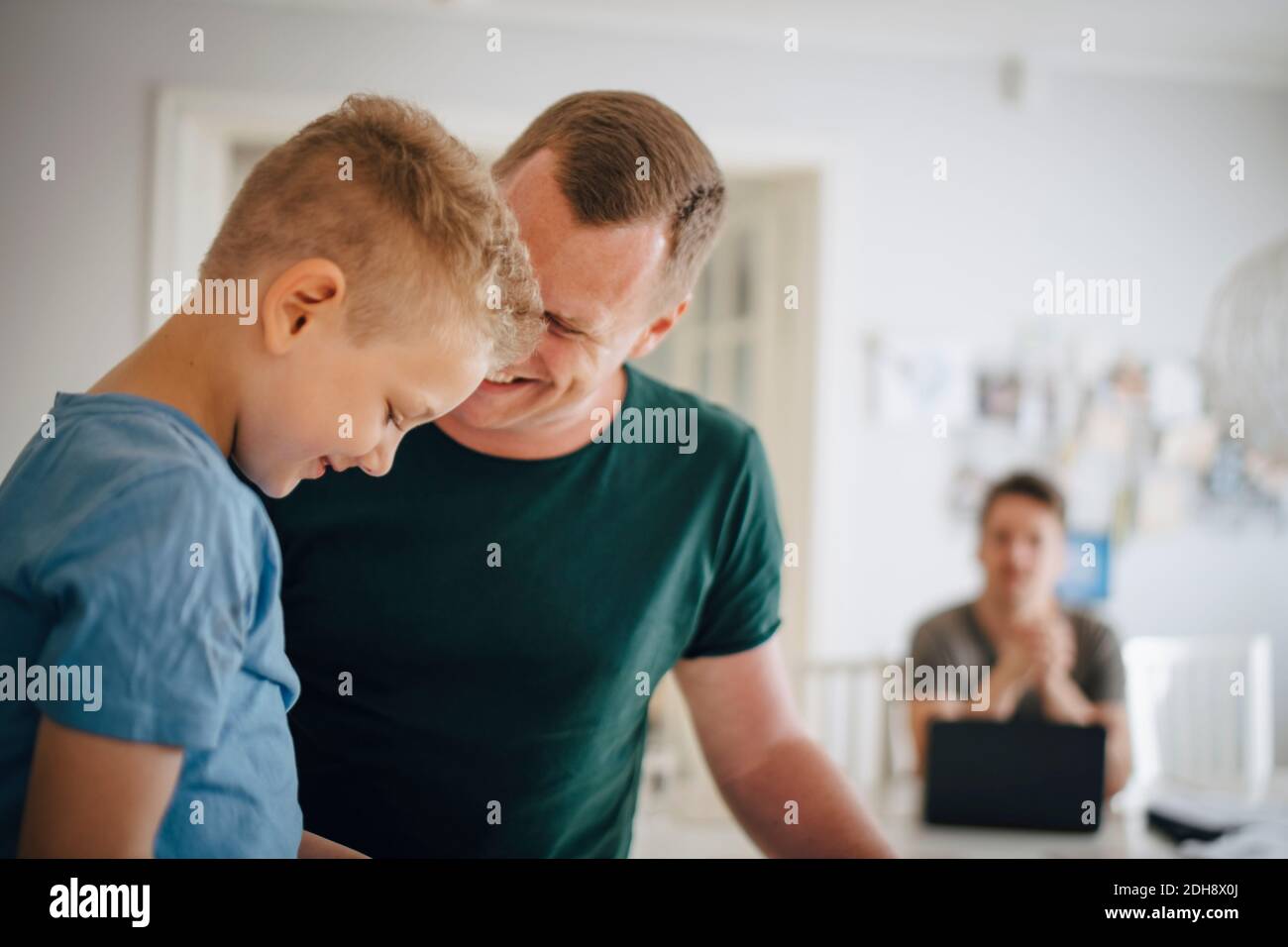 Smiling father looking at son sitting in domestic kitchen Stock Photo