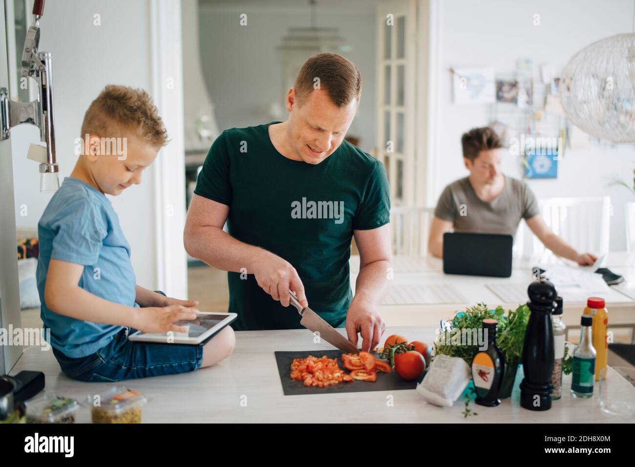 Father cutting tomato while son using digital tablet on kitchen counter Stock Photo