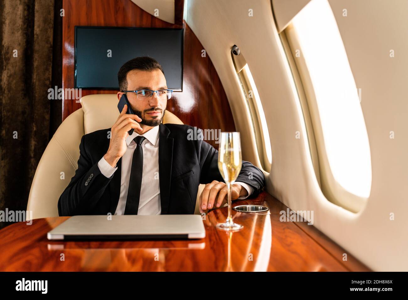 Handsome businessman wearing elegant suit  flying on exclusive private jet - Successful entrepreneur sitting in exclusive business class on airplane, Stock Photo