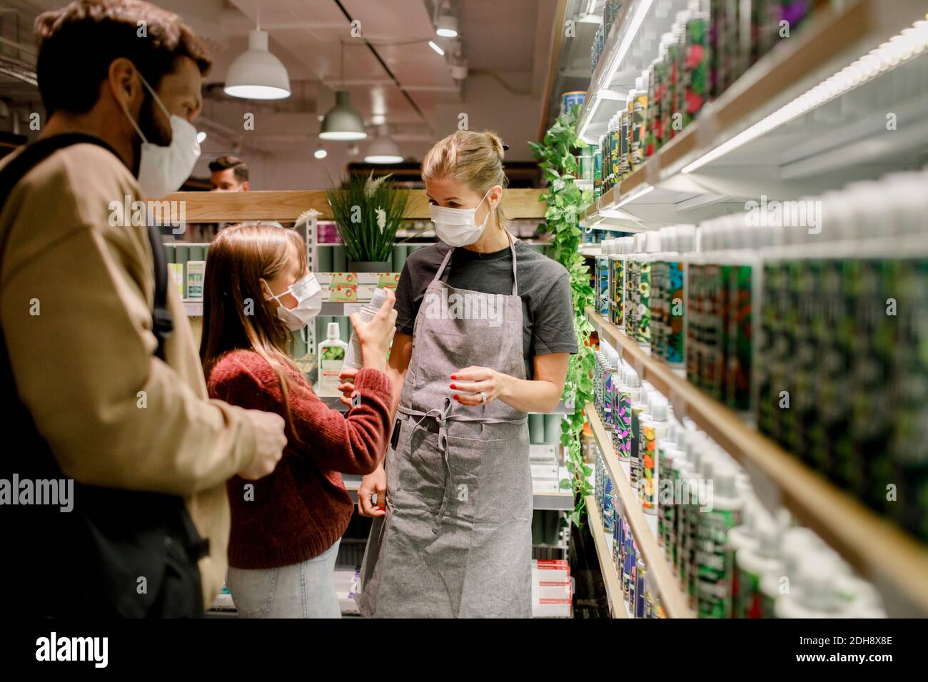 Girl talking to saleswoman by father in supermarket during COVID-19 Stock Photo