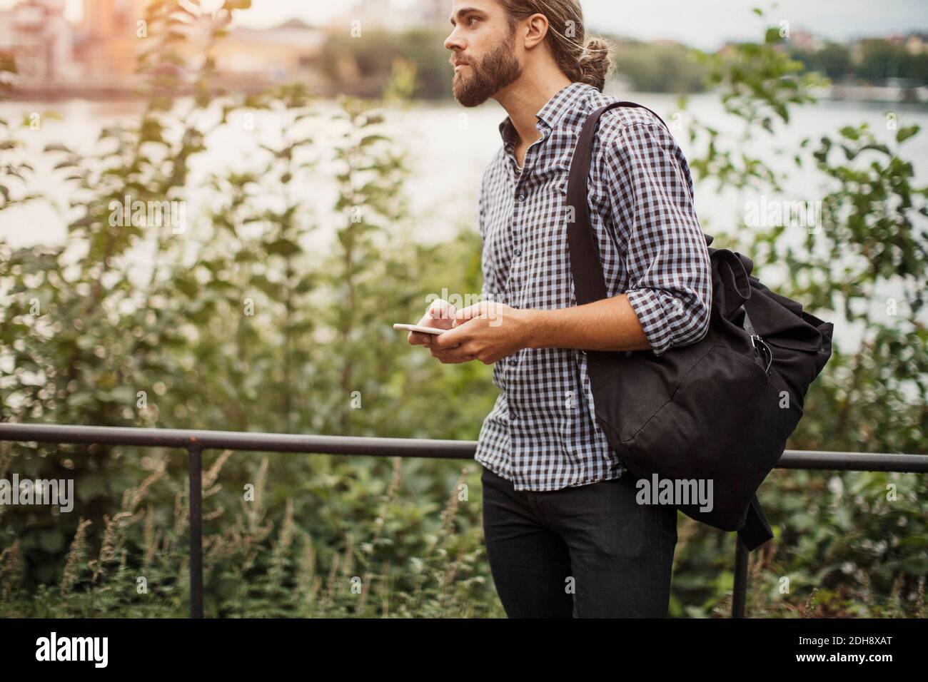 Man holding smart phone while standing by railing and plants Stock Photo