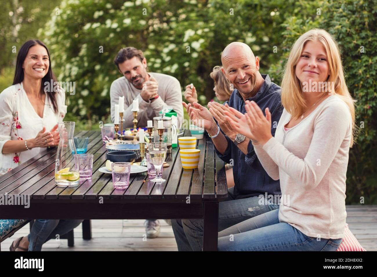 Happy family and friend applauding while sitting at dining table in back yard during garden party Stock Photo