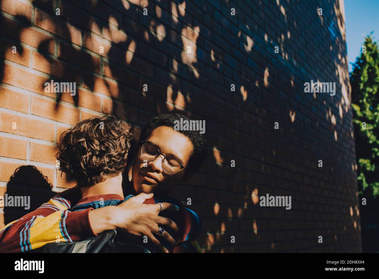 Teenager consoling friend while embracing against brick wall Stock Photo