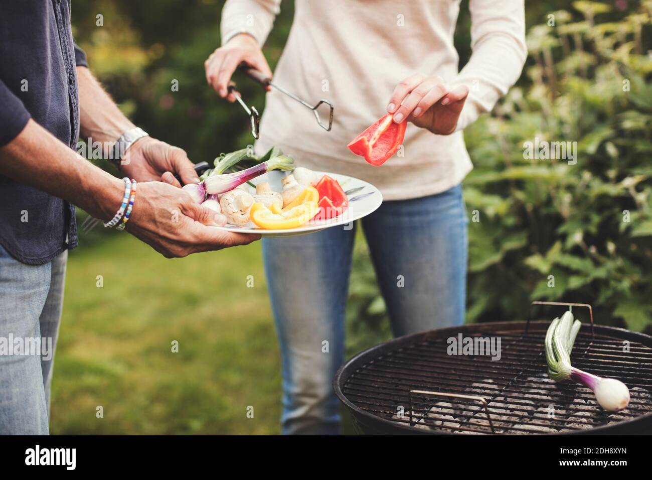 Midsection of father and daughter cooking vegetables on barbecue grill in back yard Stock Photo