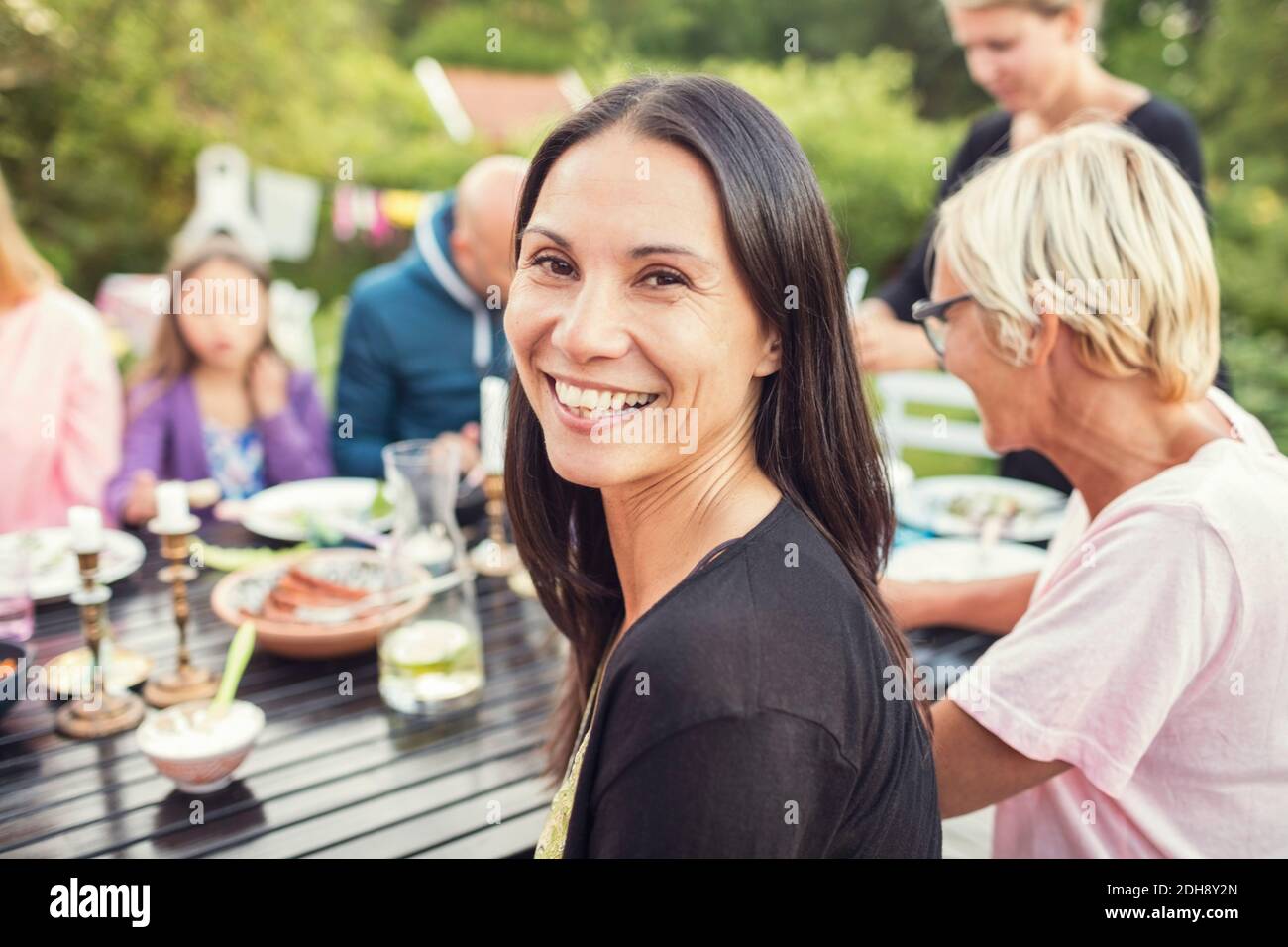Portrait of happy woman sitting with family and friends at dining table in back yard during garden party Stock Photo