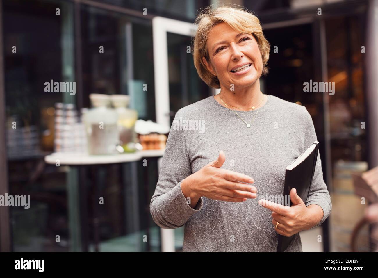 Happy businesswoman gesturing while standing at sidewalk cafe Stock Photo