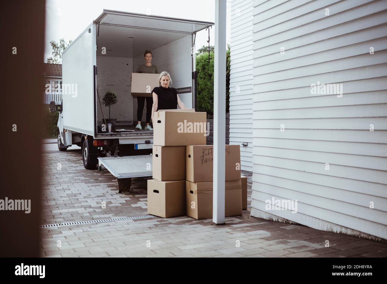Female friends unloading boxes from van Stock Photo