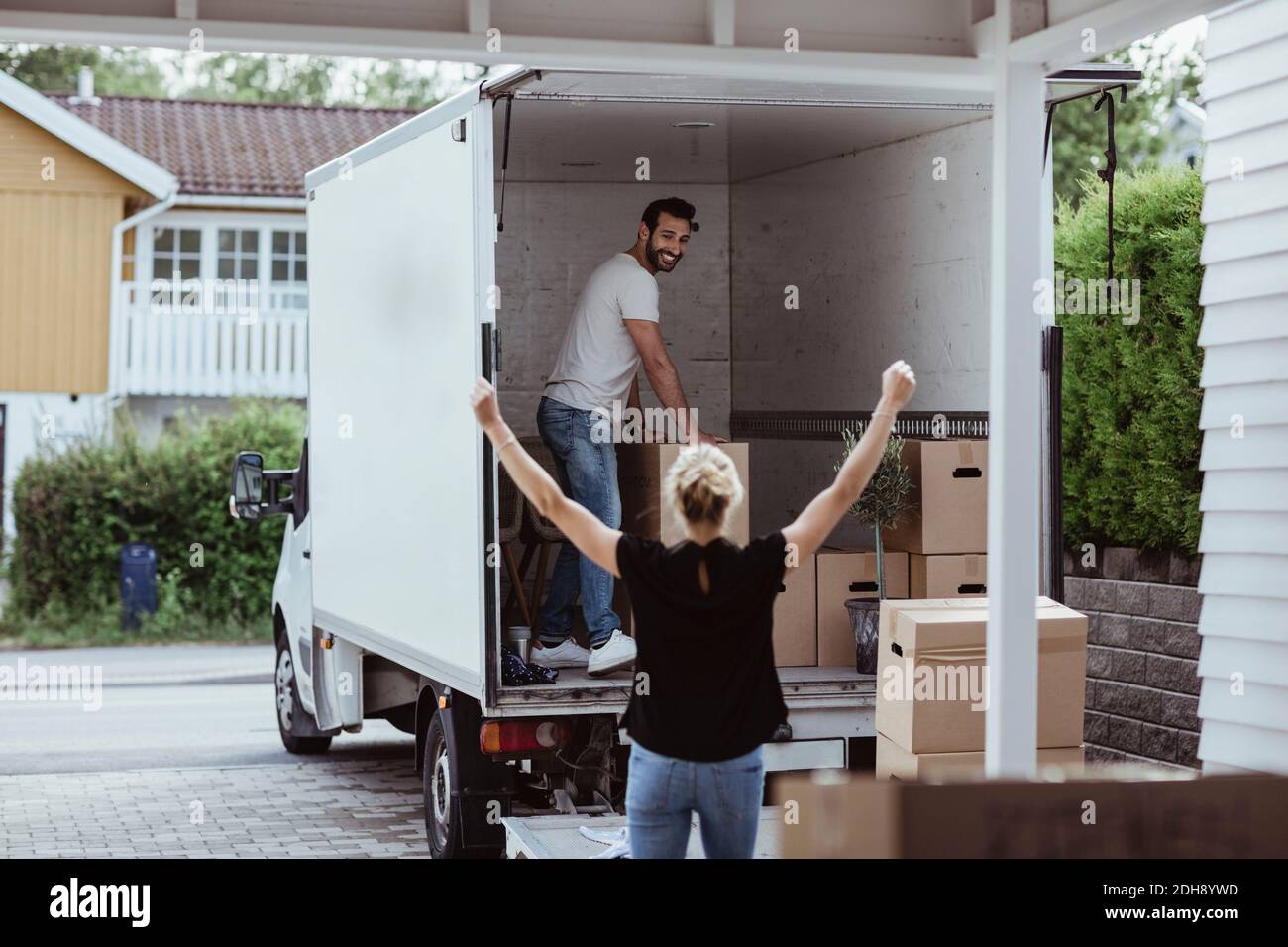 Rear view of female with arms raised cheering while smiling male partner unloading boxes Stock Photo