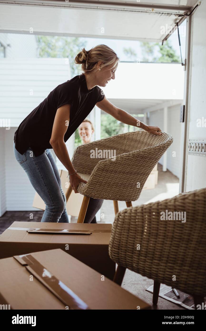 Smiling woman carrying chair while unloading during relocation Stock Photo