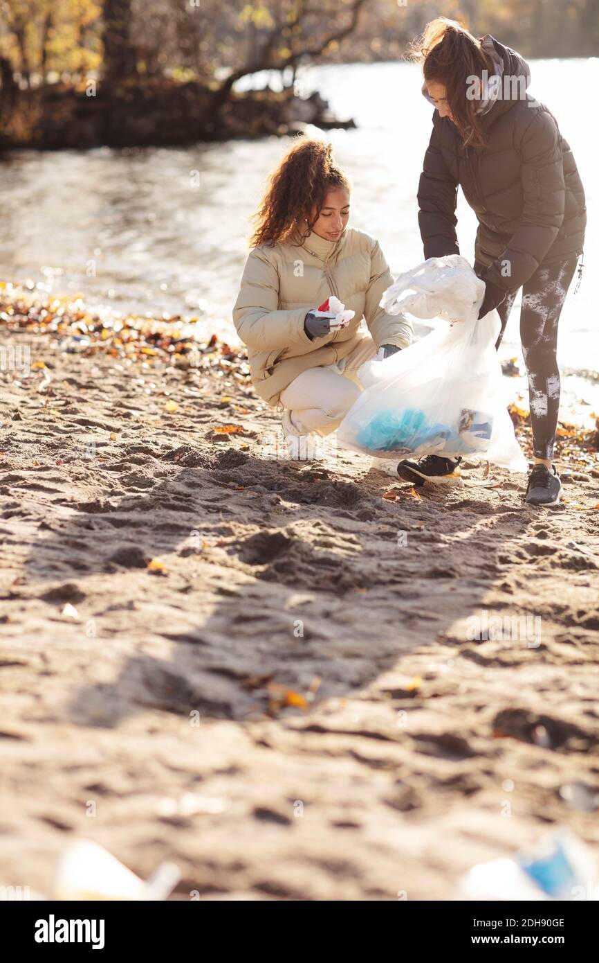 Young female environmentalist with teenage girl collecting waste while crouching on land Stock Photo