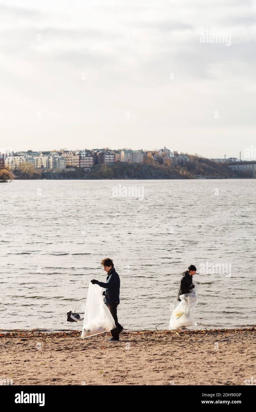 Young male environmentalists collecting plastic waste by lake against clear sky Stock Photo